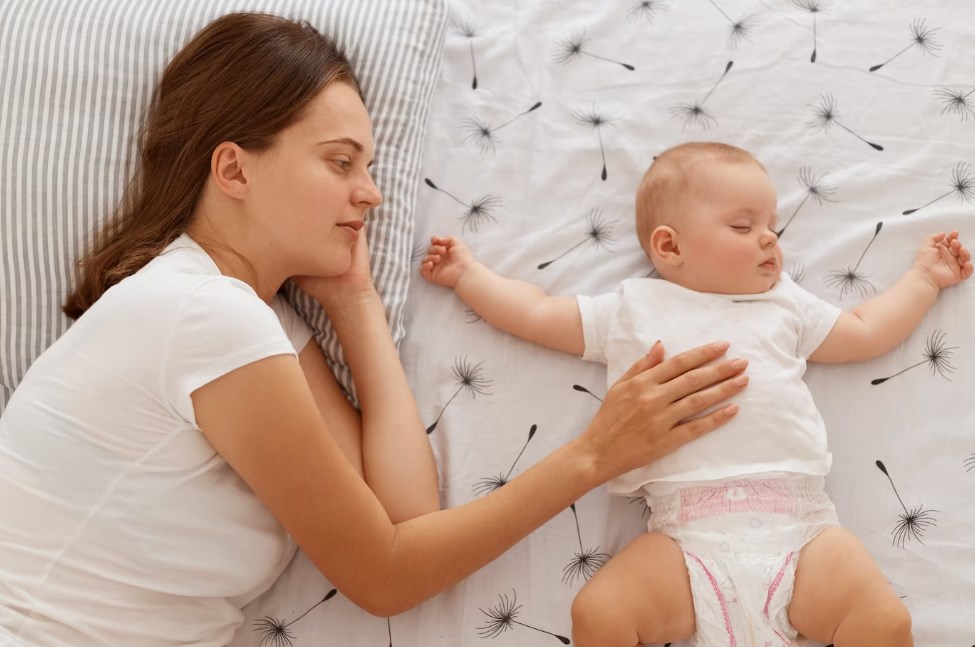 a top view of a woman in a white t-shirt laying on a bed with an infant