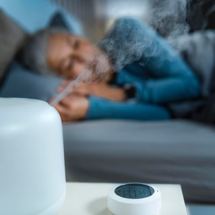 an air humidifier and a home humidity sensor on the nightstand in a bedroom with a sleeping woman in the background