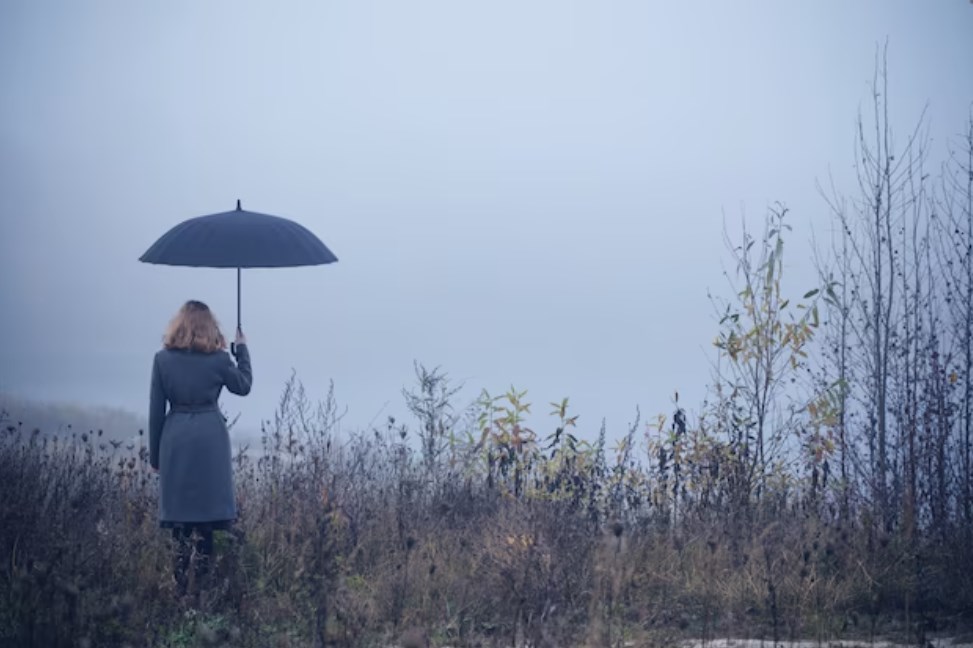 a woman wearing a grey coat with an umbrella in an autumn field