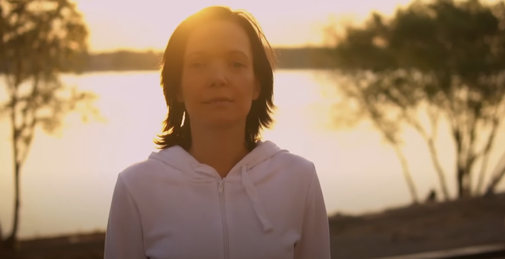 A female looking at the camera with the sun shining brightly behind her.