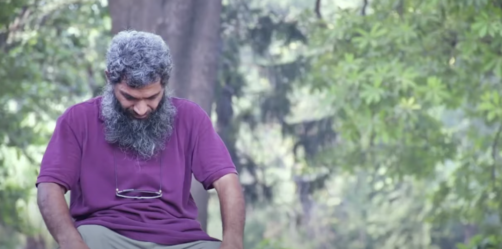 Image of a man sitting with his head down, dressed in purple.