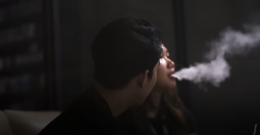 A girl exhaling smoke while a guy looks at her