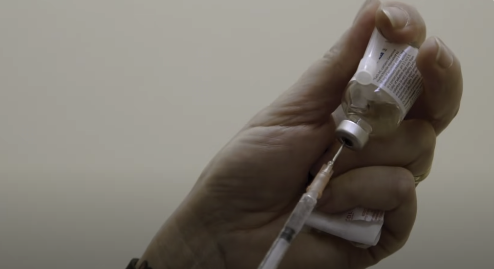 Hand holding an inverted small bottle and extracting liquid using a syringe.