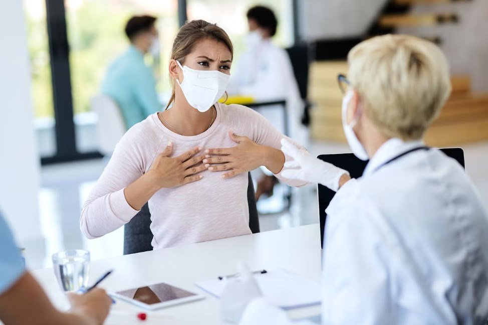 a young woman explaining that she feels a strong pain in her chest to a female doctor