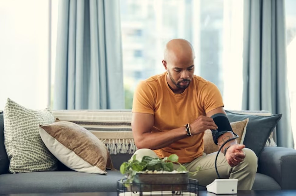 a shot of a black man checking his blood pressure while sitting on a sofa