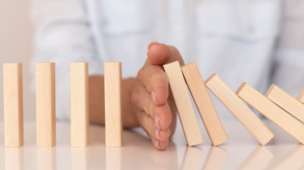 a hand stopping small wooden blocks from falling down in a chain reaction on a table