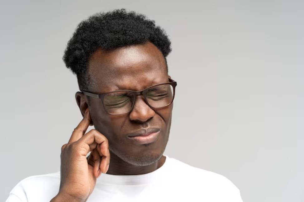 a black man frowning and suffering from tinnitus throbbing earache while touching his ear