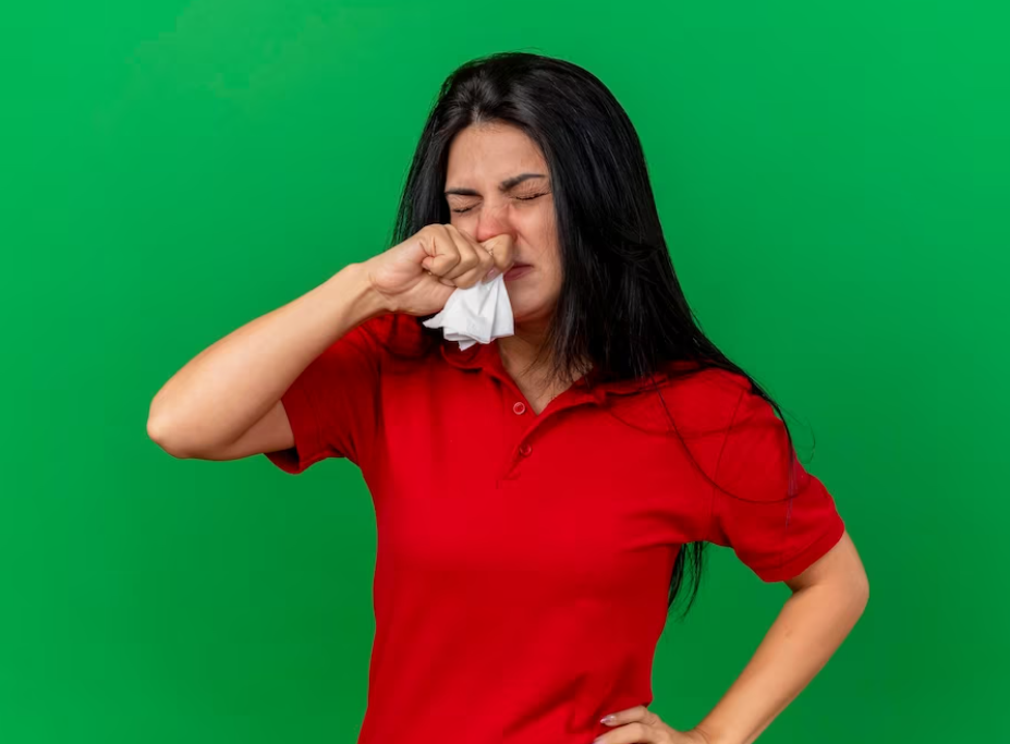 woman in red t-shirt wipes her nose with napkins in front of green wall