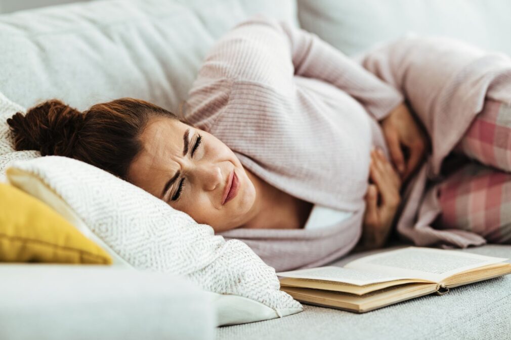 Woman feeling pain in her abdomen while lying down on sofa